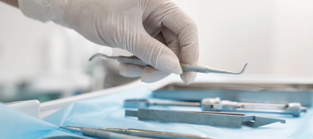 Mãos com luva segurando os instrumentos de Odonto